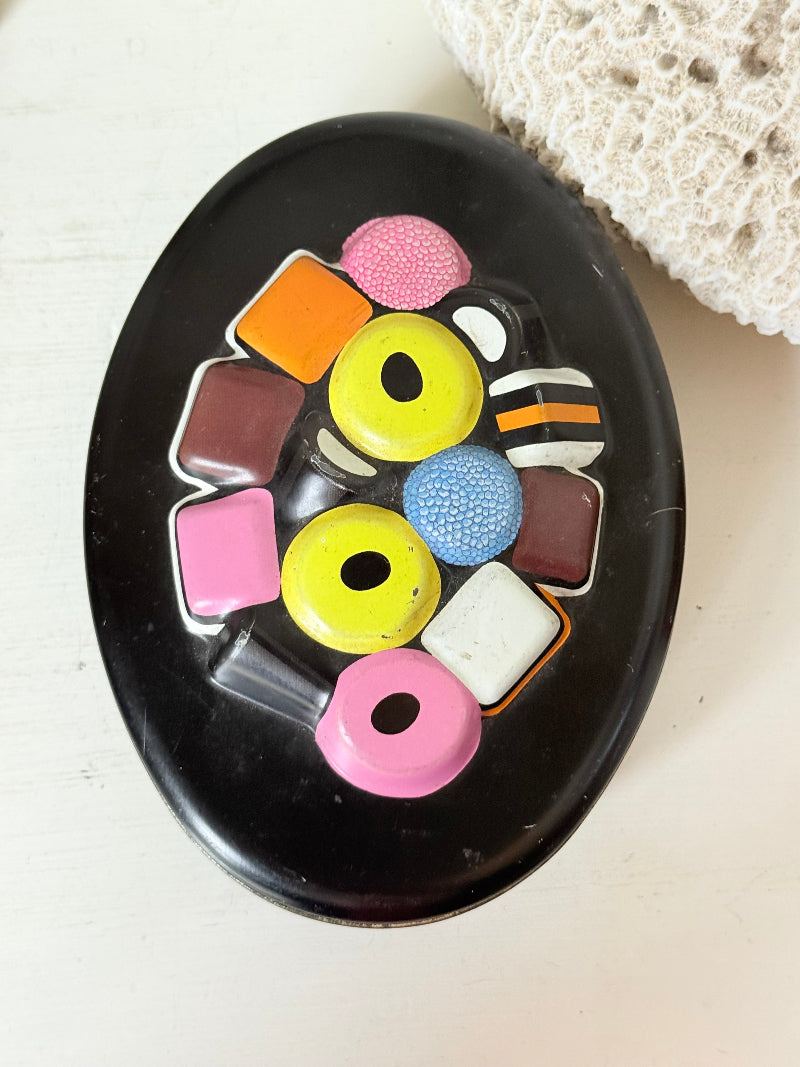 Vintage Liquorice Allsorts decorative tin with raised multicolour sweet design on black base, photographed on white surface.