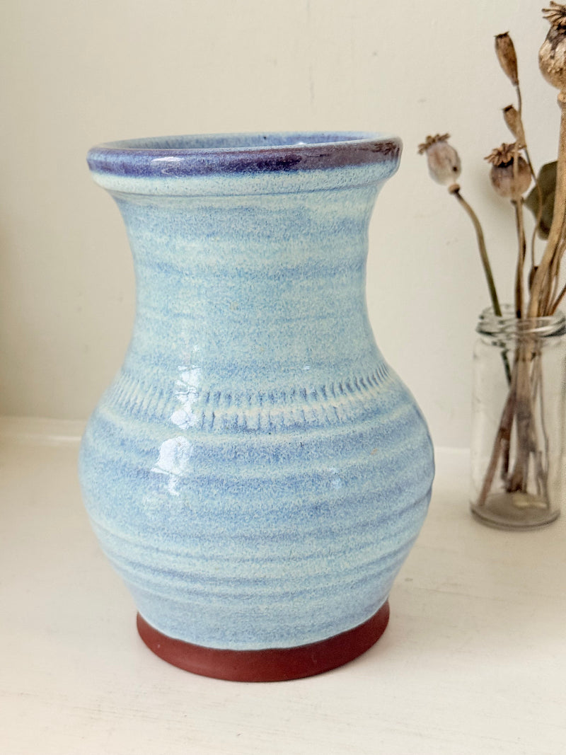 Studio pottery vase with sky blue glaze, indigo rim, and natural red clay base, photographed on a white surface
