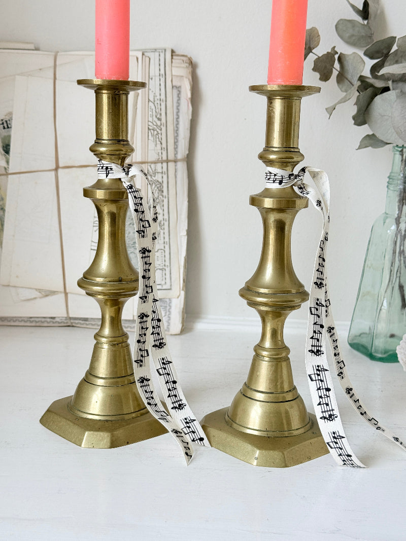 Pair of antique brass candlesticks with turned baluster stems and stepped bases holding coral tapers