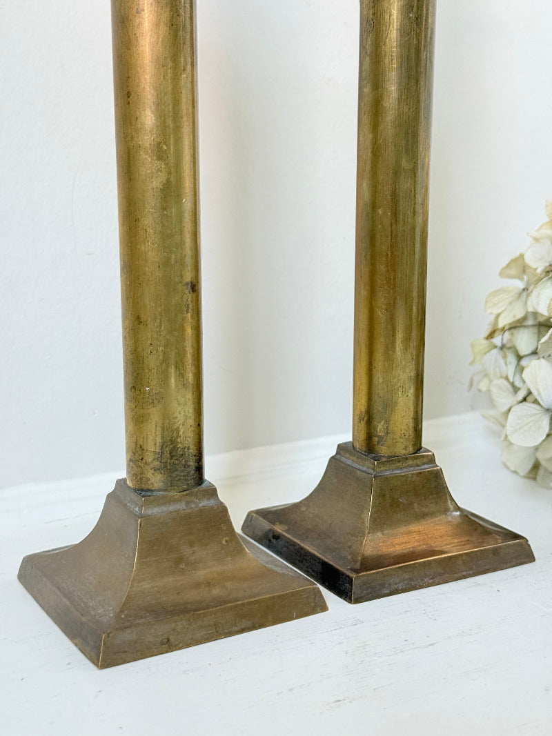 Pair of vintage brass candlesticks with square bases and white taper candles, styled on a white surface beside dried hydrangeas.