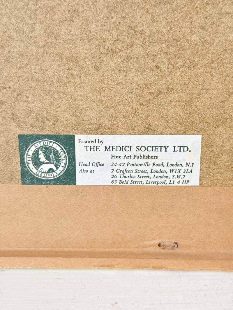 Close-up of the back of a framed art print or painting, showing a brown cardboard backing with a white label that reads &