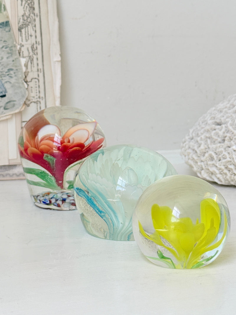 Trio of vintage glass paperweights with red flower, yellow flower and turquoise swirl decoration in clear coloured glass