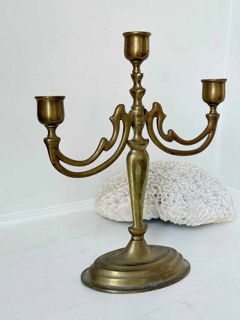 Vintage brass three-arm candelabra with curved arms and soft patina, photographed on a white surface