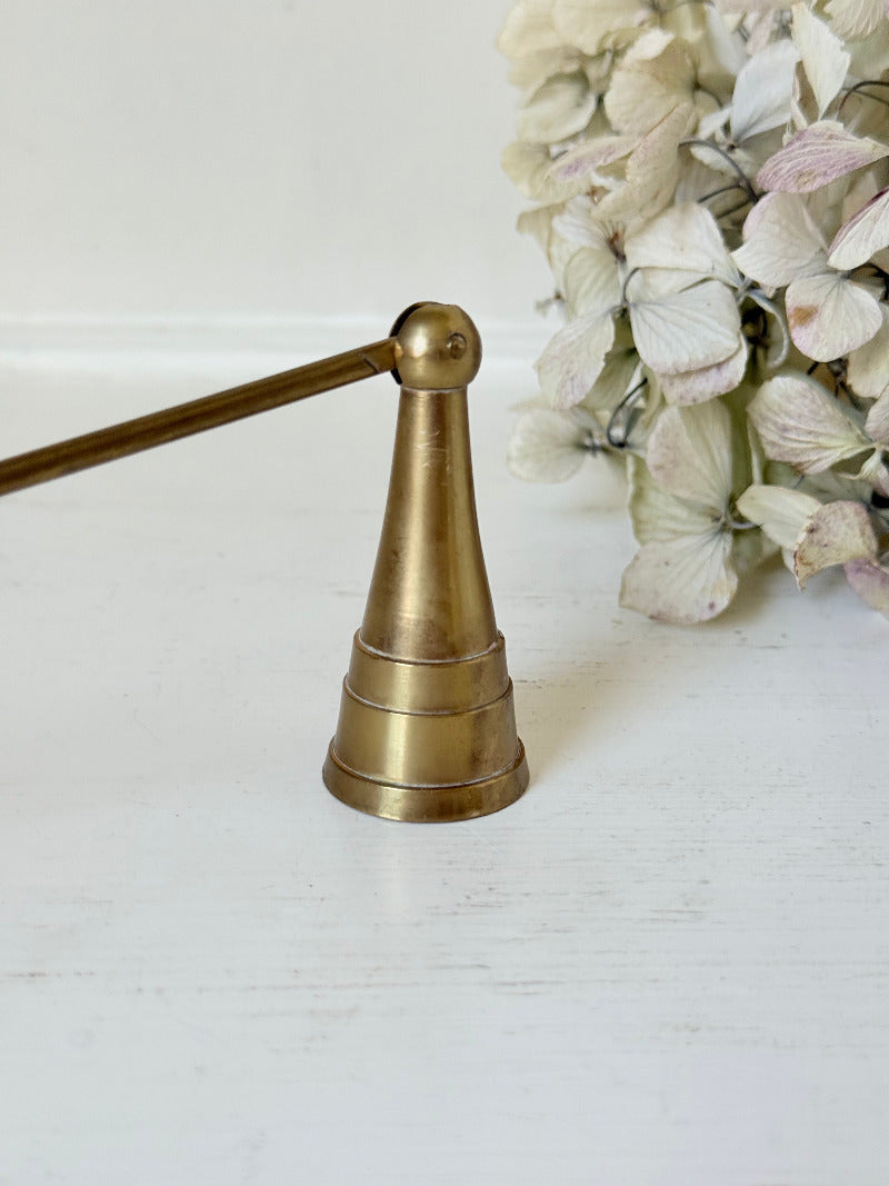 vintage brass candle snuffer with twisted handle and cone-shaped head photographed on white surface