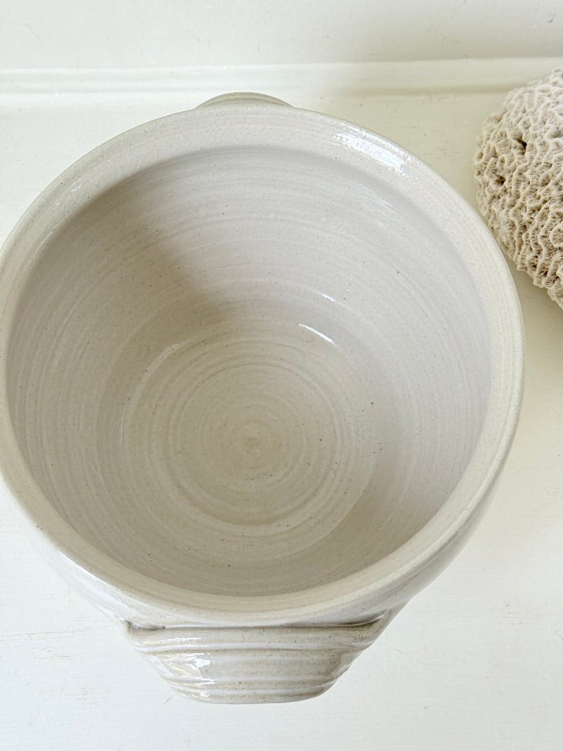 Large studio pottery bowl with hand-painted grape motif and side handles, photographed on a white surface