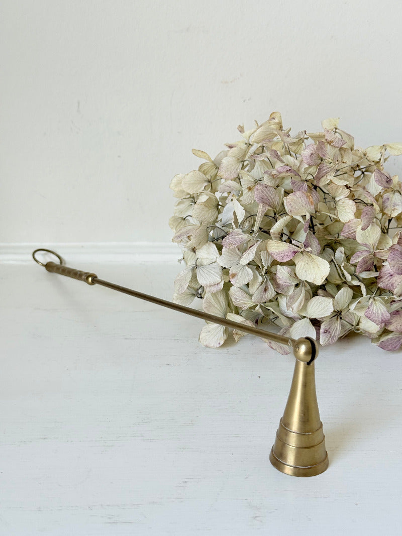 vintage brass candle snuffer with twisted handle and cone-shaped head photographed on white surface
