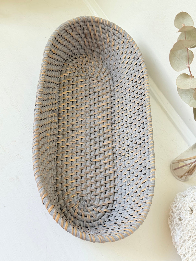 Vintage grey woven bread basket with oval shape and raised rim, photographed on white surface.