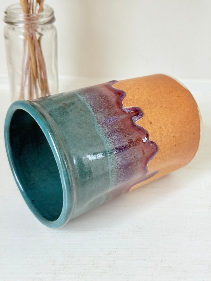 Studio pottery pen pot with teal and plum drip glaze, photographed on a white surface