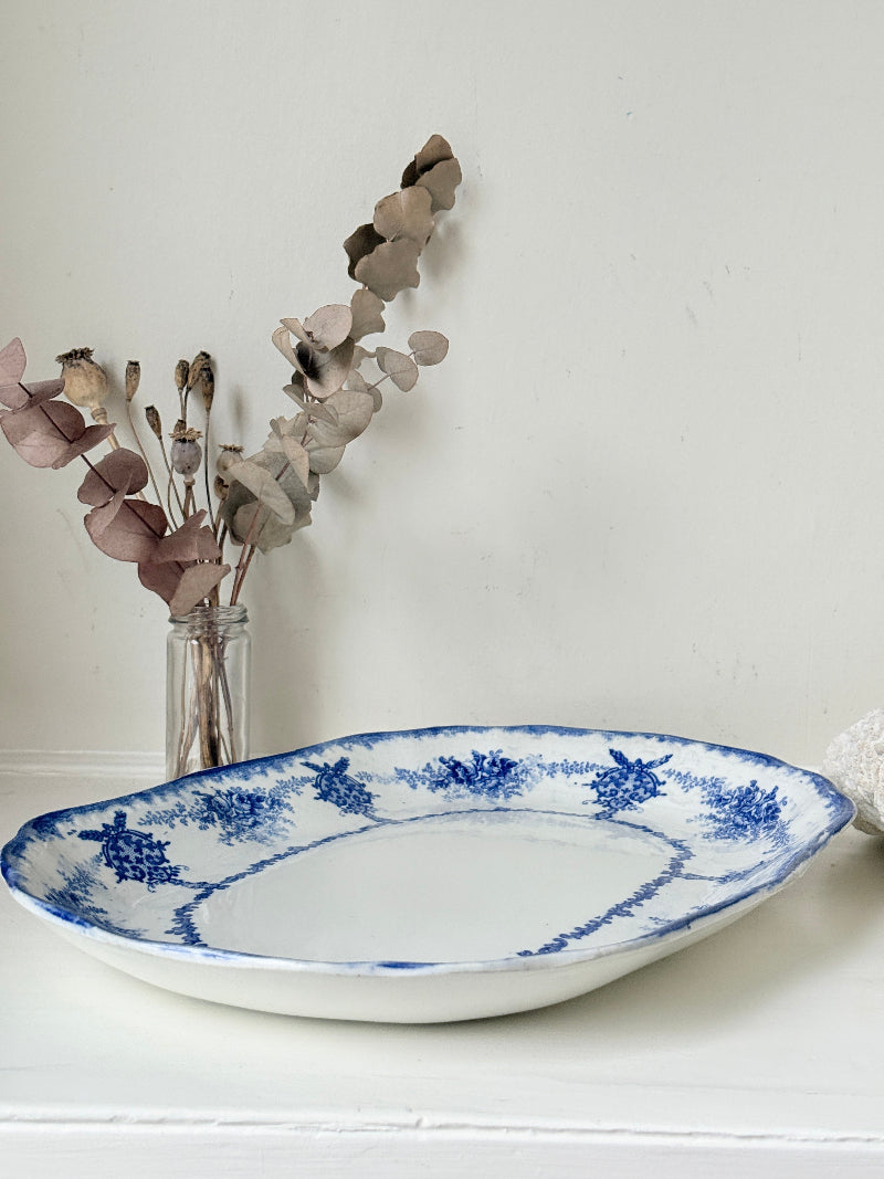 Antique oval blue and white platter with floral border photographed on a white surface