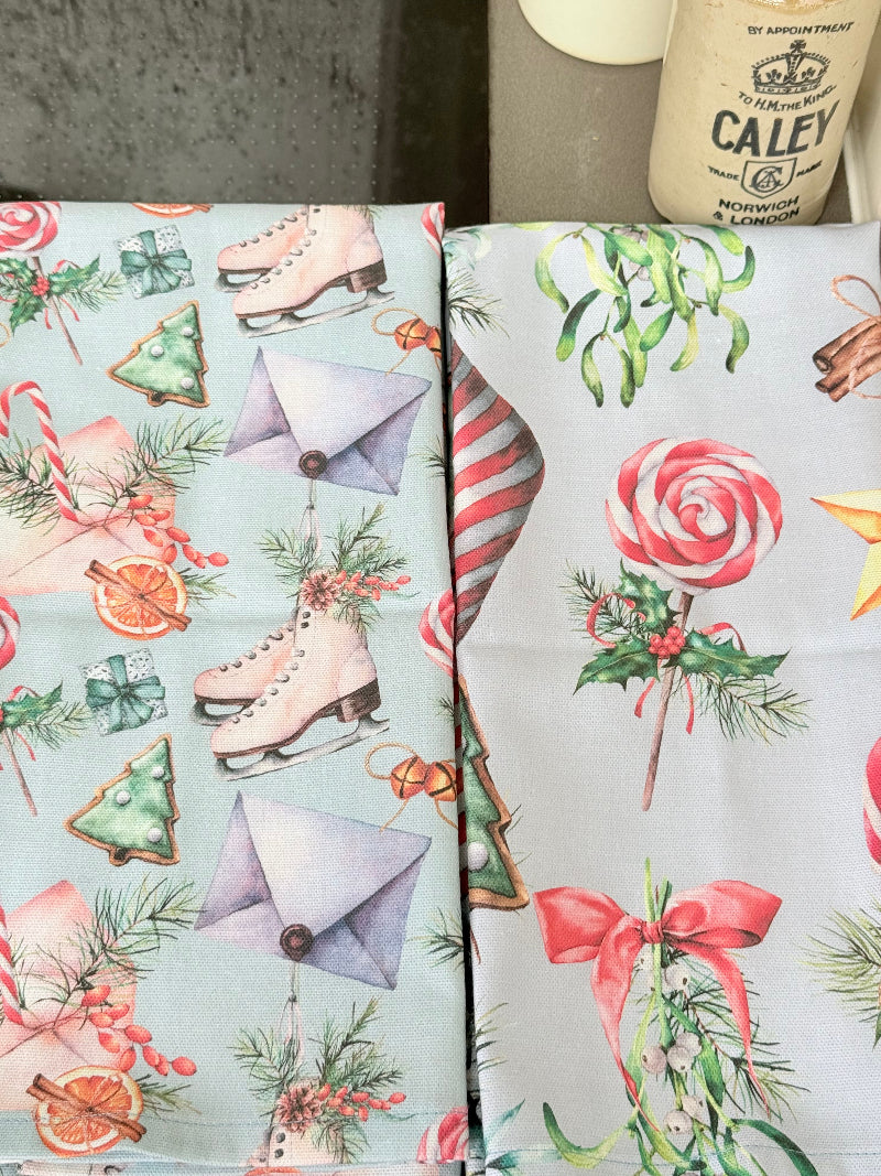 Pair of pastel blue festive tea towels with candy cane and ribbon print, folded, photographed on a kitchen worktop