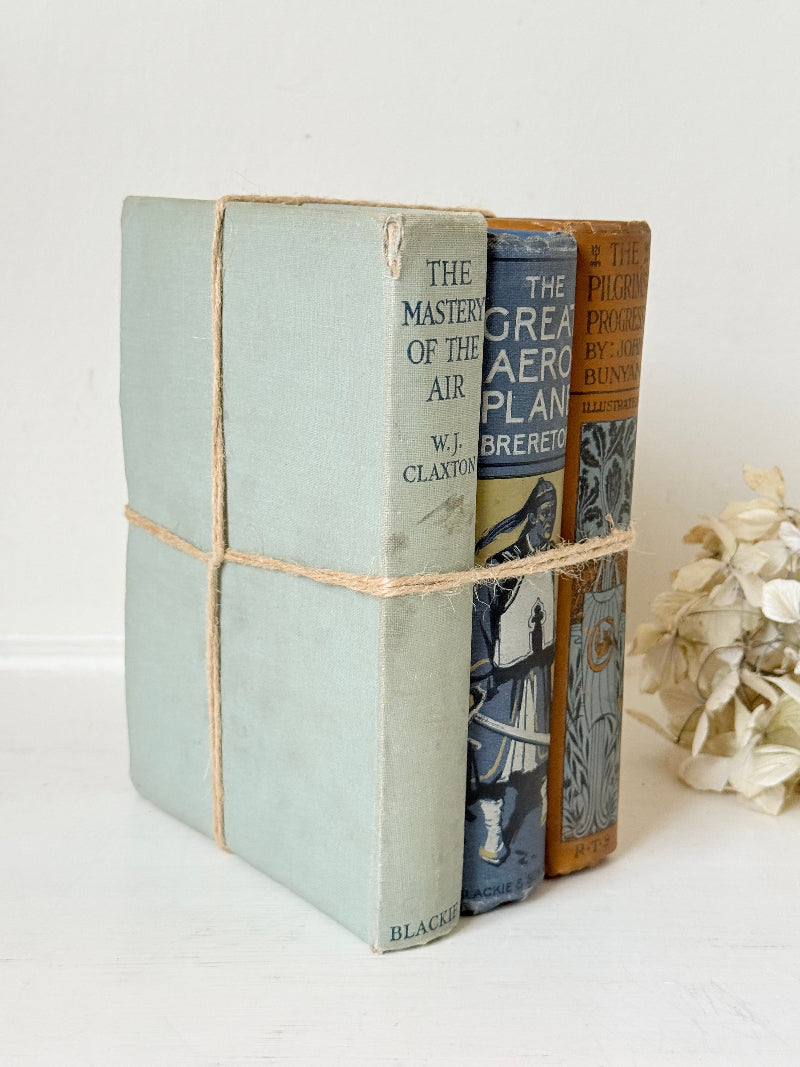 Vintage decorative book bundle in blue, grey, and ochre tied with twine, photographed on a white surface