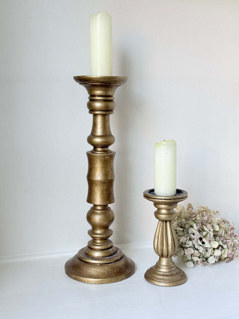 Pair of vintage wooden candlesticks, one tall and one small, in golden-toned finish, styled with pillar candles on a white surface.