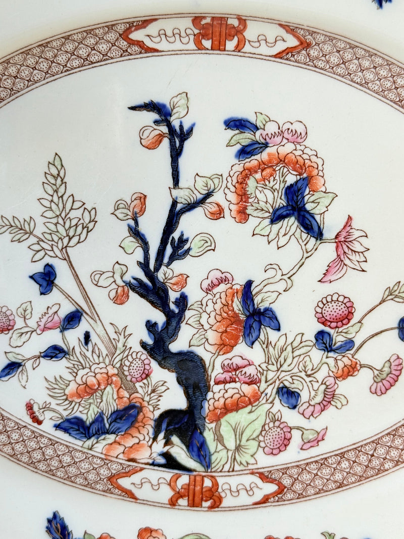 Vintage oval serving platter with chinoiserie style blue and red pattern photographed on a white surface