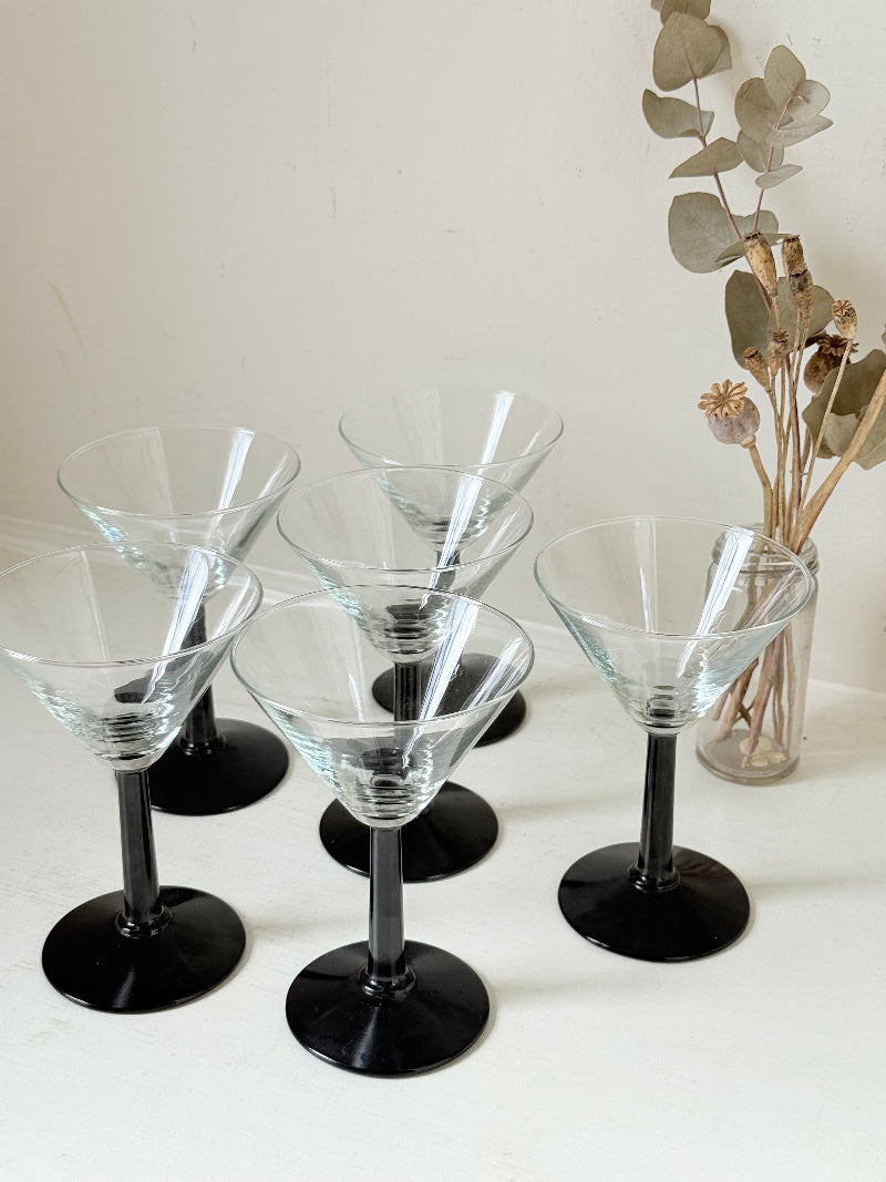 Set of six clear martini glasses with black stems, photographed on a white surface