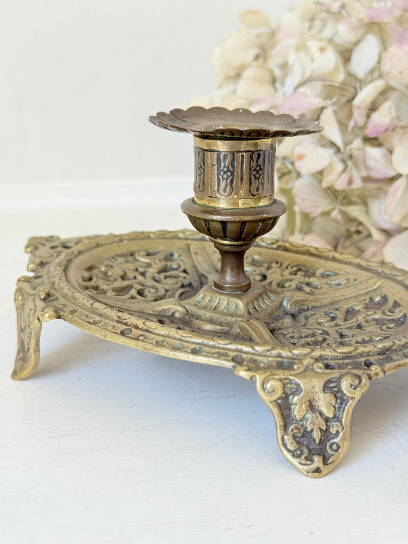 Ornate vintage brass candlestick with decorative handle and footed base, photographed on a white surface