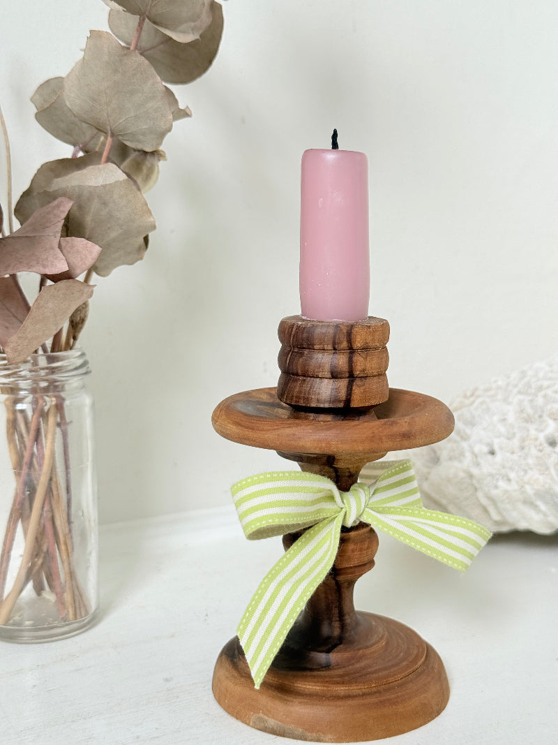 Vintage olivewood candlestick photographed on a white surface, turned wooden stem with warm grain and wide base holding a pink taper candle
