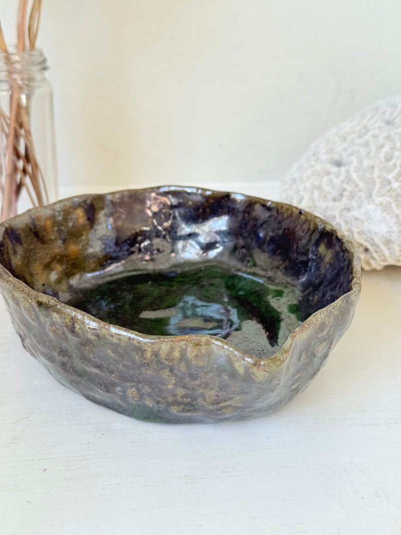 Studio pottery olive bowl with green and charcoal glaze, photographed on a white surface