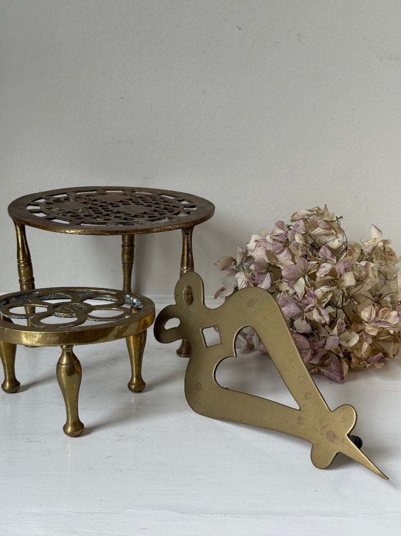 Vintage brass trivet trio with ornate cutwork designs and aged patina, photographed on a white surface