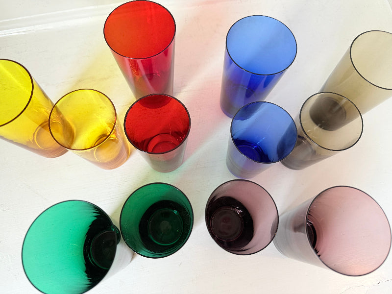 Set of six mid-20th century Boussu coloured glass beakers in rainbow hues, green with original label, photographed on white surface.