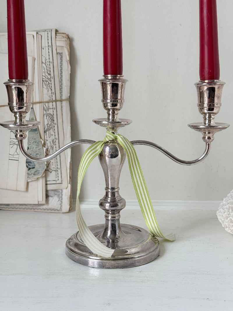 Silver plate three light candelabra with curved arms and domed base holding red taper candles