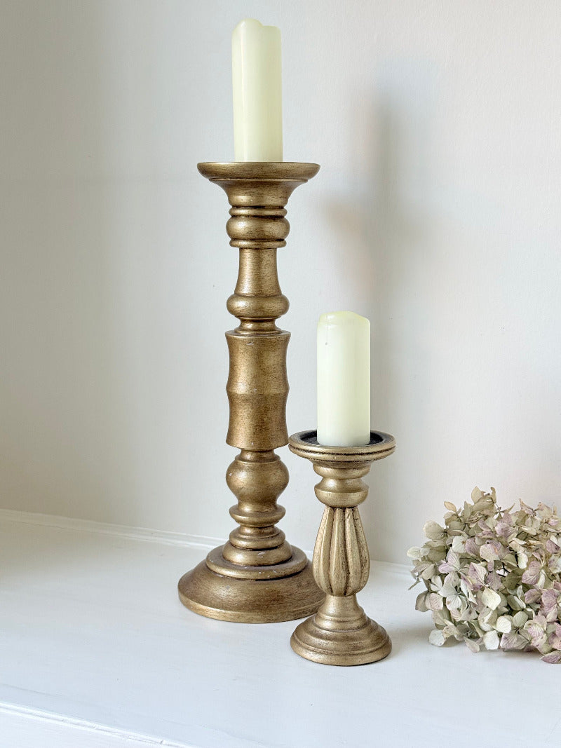 Pair of vintage wooden candlesticks, one tall and one small, in golden-toned finish, styled with pillar candles on a white surface.