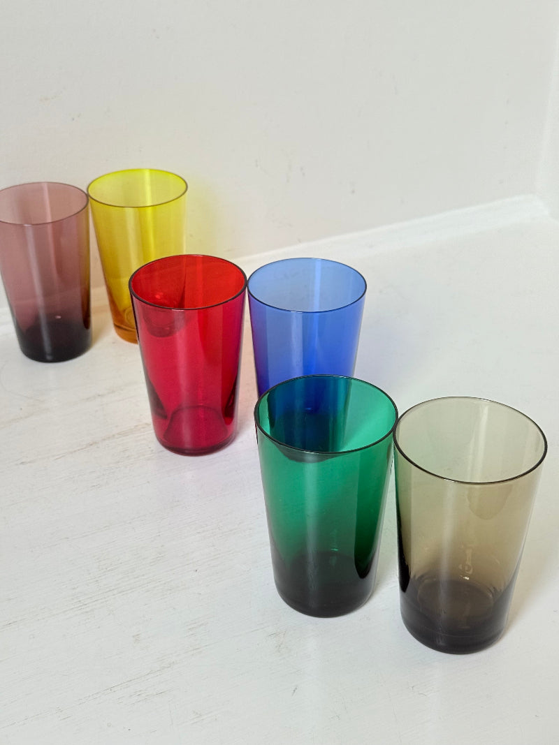 Set of six mid-20th century Boussu coloured glass beakers in rainbow hues, green with original label, photographed on white surface.