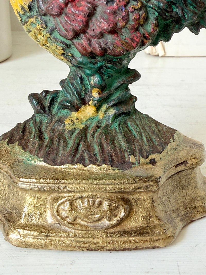 Close-up of a vintage cast iron money box featuring a detailed floral design in green, red, and yellow, with a textured gold-toned base.