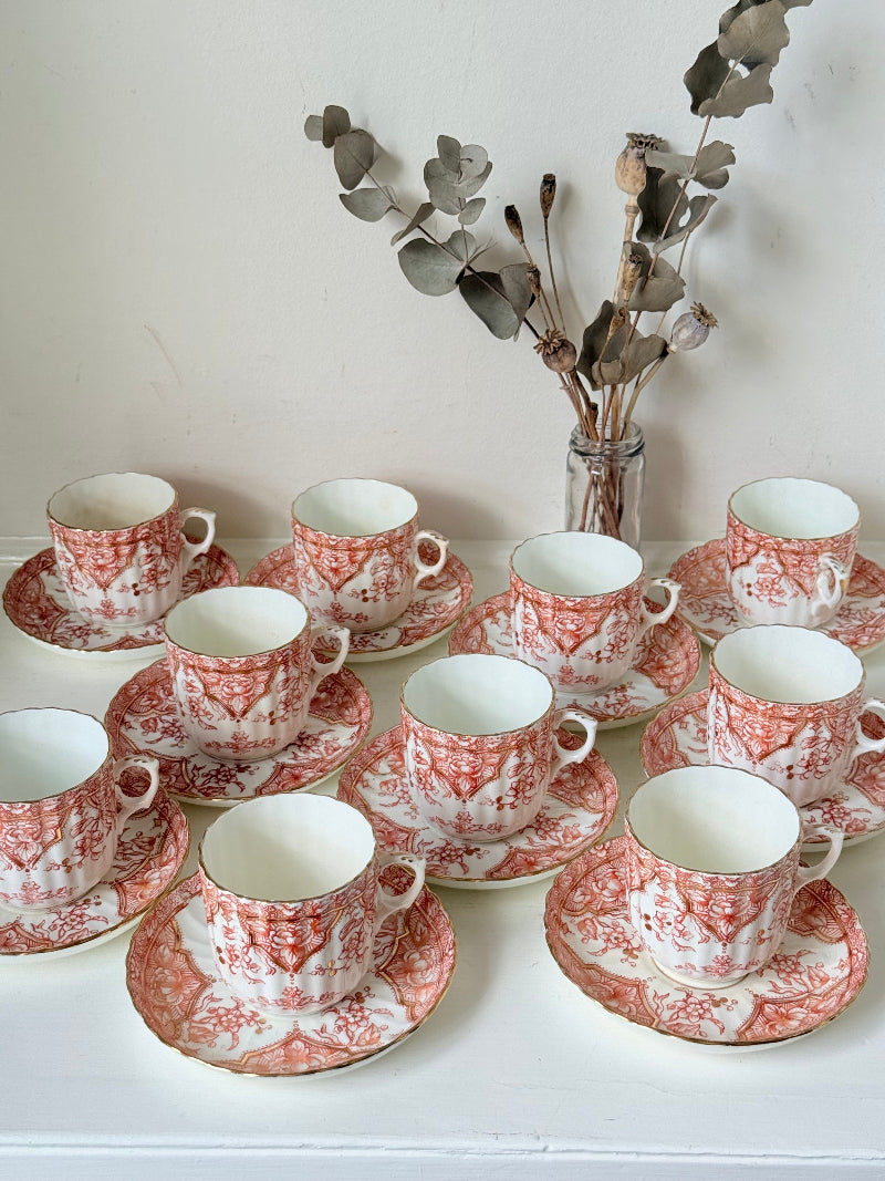 Vintage coral transferware coffee cans and saucers with scalloped edges and gold accents, set of ten, styled on a white surface.