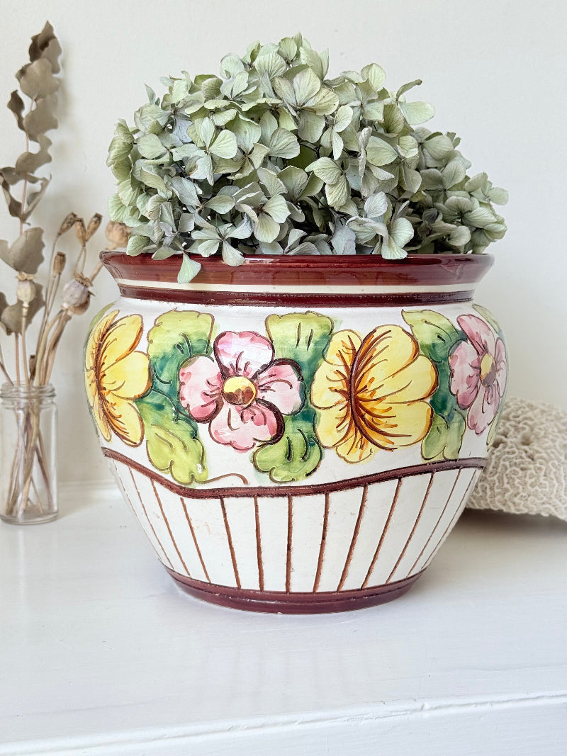 Large European hand painted floral ceramic jardinière with yellow, pink and green flowers on a white base, styled on a white surface with dried foliage.