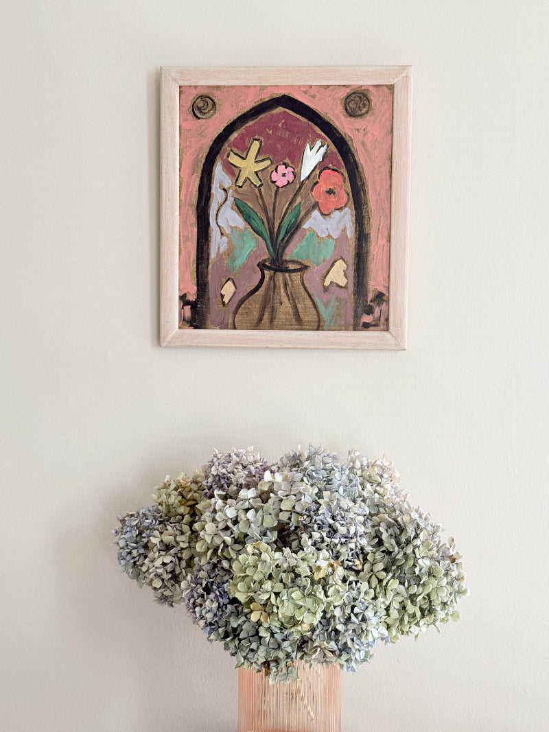 Modern British School oil on board painting of stylised flowers by a gothic arch in a pale frame, photographed against a light wall