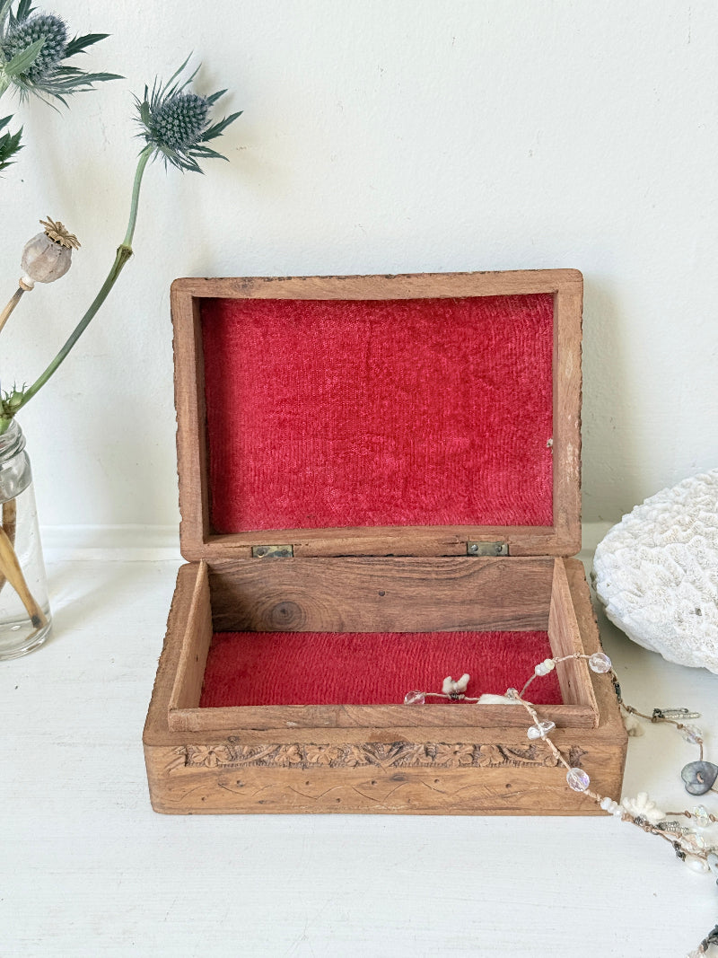 Vintage hand carved wooden jewellery box with floral detail and red fabric lining, photographed on a white surface