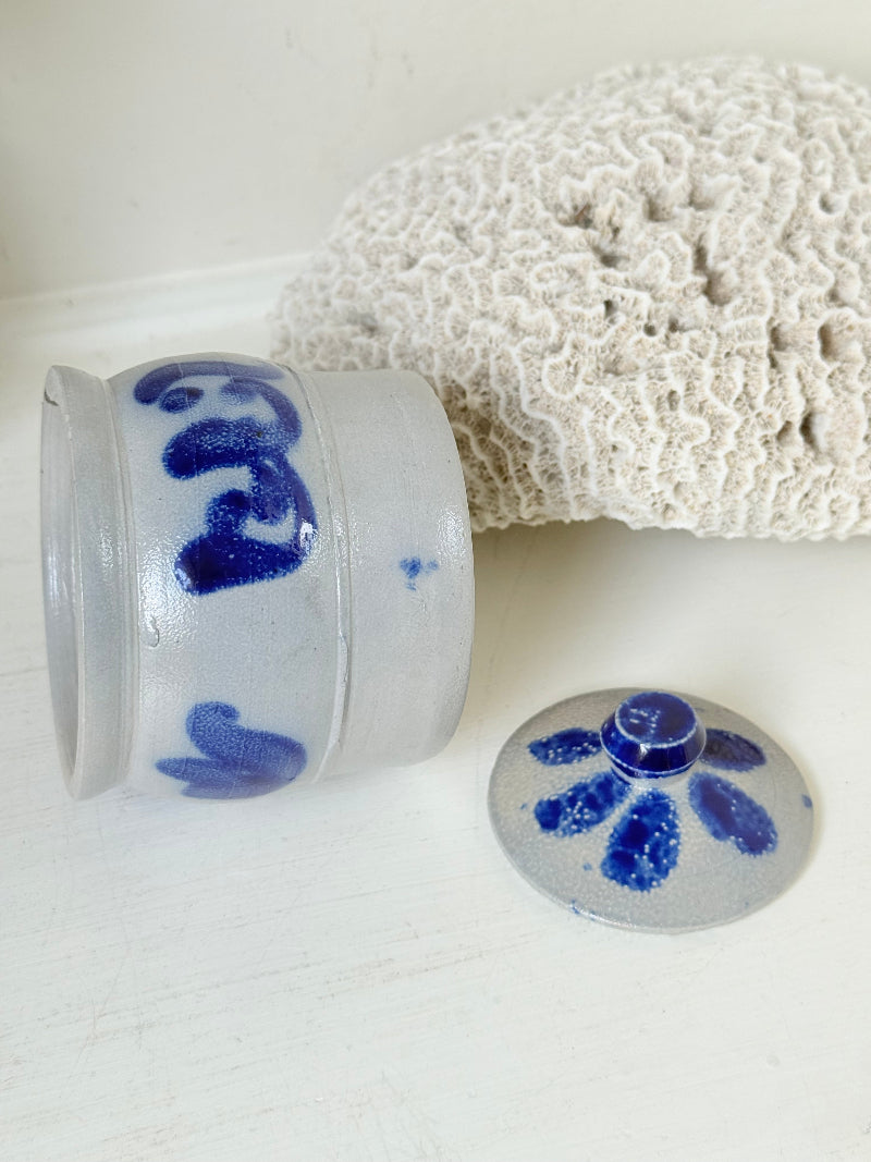 Vintage lidded pottery jar with hand painted blue floral decoration, photographed on a white surface