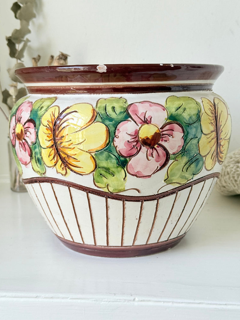 Large European hand painted floral ceramic jardinière with yellow, pink and green flowers on a white base, styled on a white surface with dried foliage.