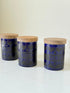 Set of three Hornsea Pottery spice jars in cobalt blue with wooden lids, labelled Ginger, Nutmeg, and Peppercorn, photographed on white surface