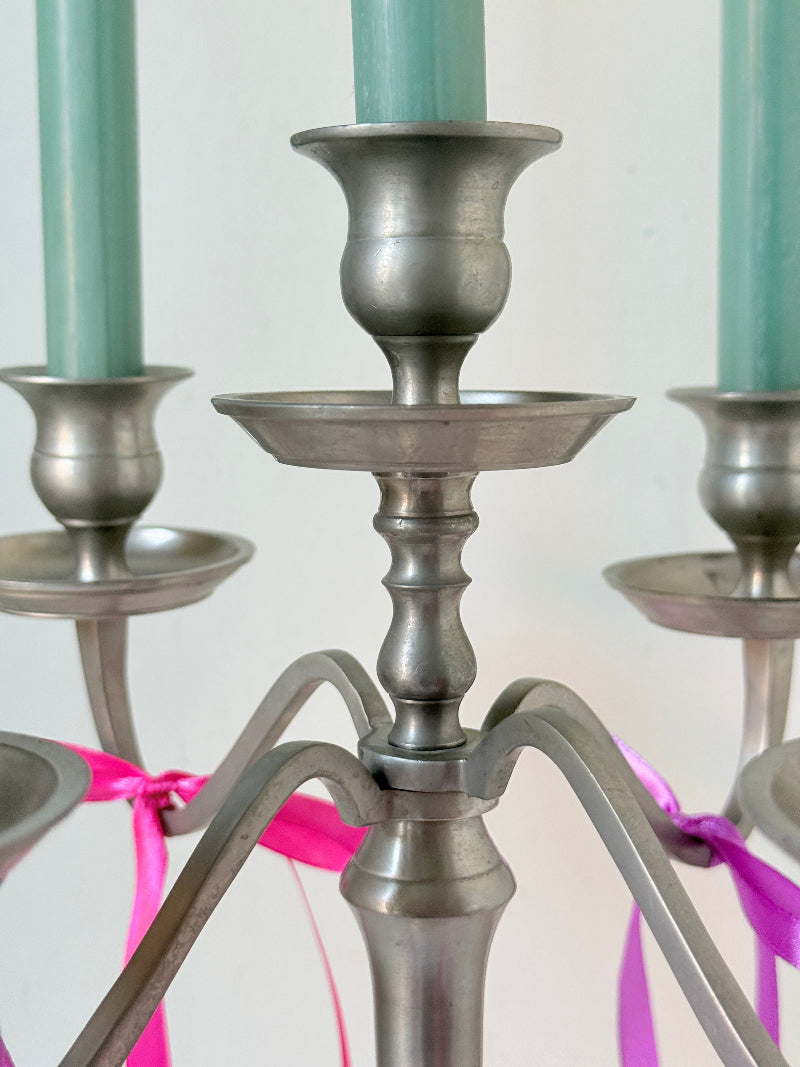 Five arm pewter style metal candelabra with aged silver finish styled with blue green taper candles on white surface