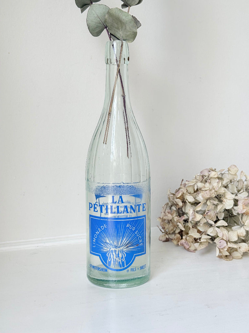 vintage french lemonade bottle la pétillante blue label on white surface with hydrangea flowers