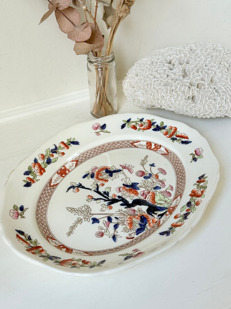 Vintage oval serving platter with chinoiserie style blue and red pattern photographed on a white surface