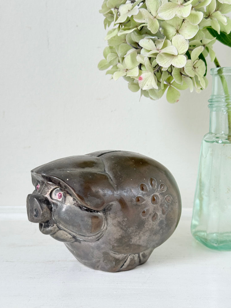 Vintage cast metal piggy bank in the shape of a pig with red painted eyes, photographed on a white surface