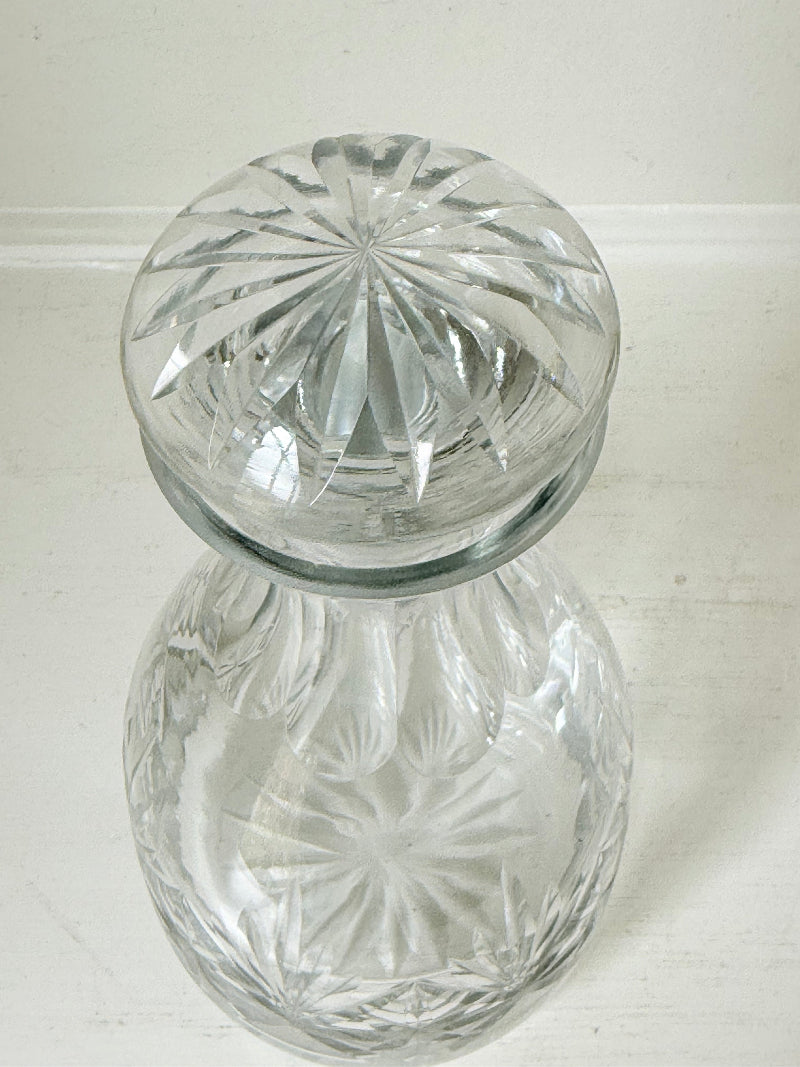 Vintage crystal decanter with faceted stopper and cut glass starburst design, photographed on a white surface