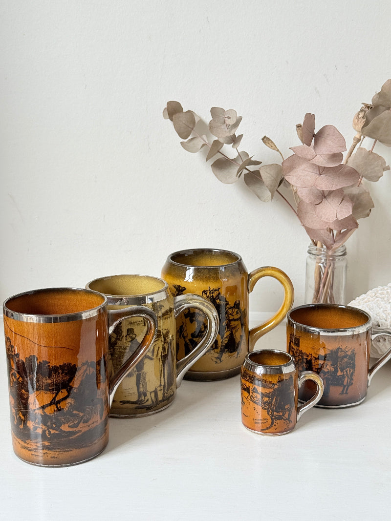 Set of 5 Ridgways stoneware mugs photographed on a white surface in amber brown glaze with black Coaching Days and Coaching Ways transfer scenes
