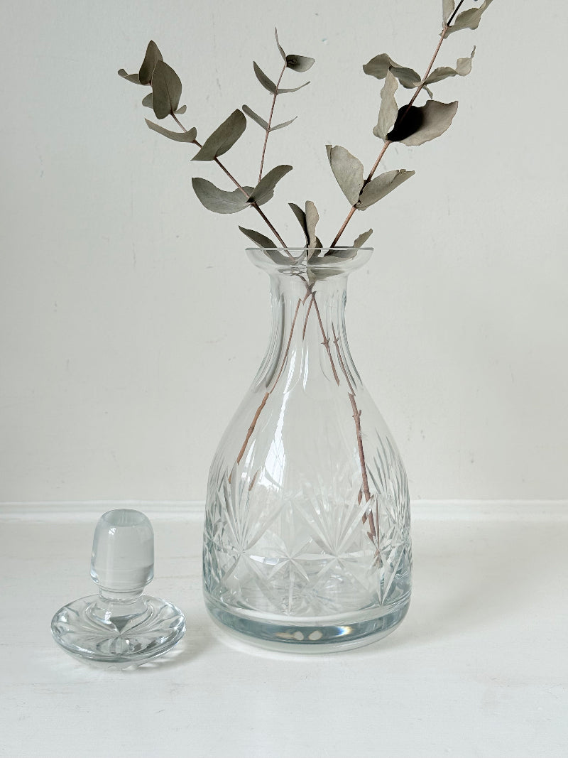 Vintage crystal decanter with faceted stopper and cut glass starburst design, photographed on a white surface