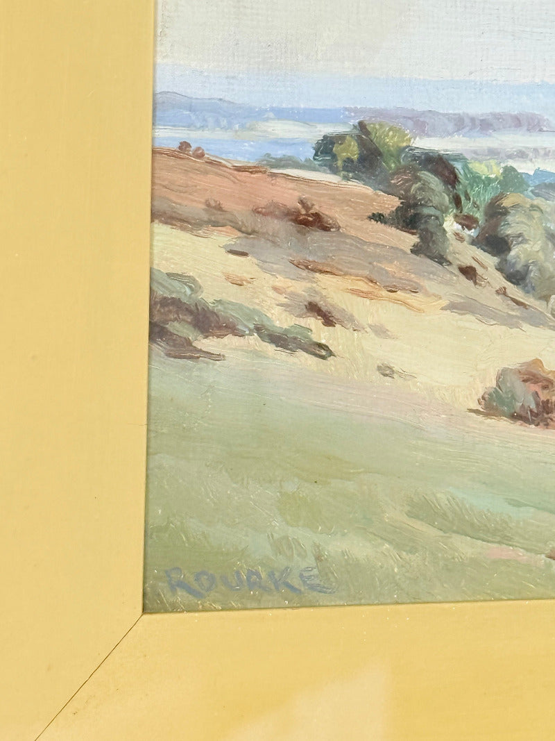 Framed oil painting of a rolling countryside landscape under a dramatic cloud-filled sky in an ornate gilt frame with wide mount.