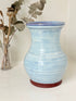 Studio pottery vase with sky blue glaze, indigo rim, and natural red clay base, photographed on a white surface