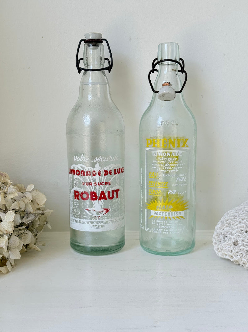 Pair of vintage French glass bottles with retro typography and graphics, photographed on a white surface