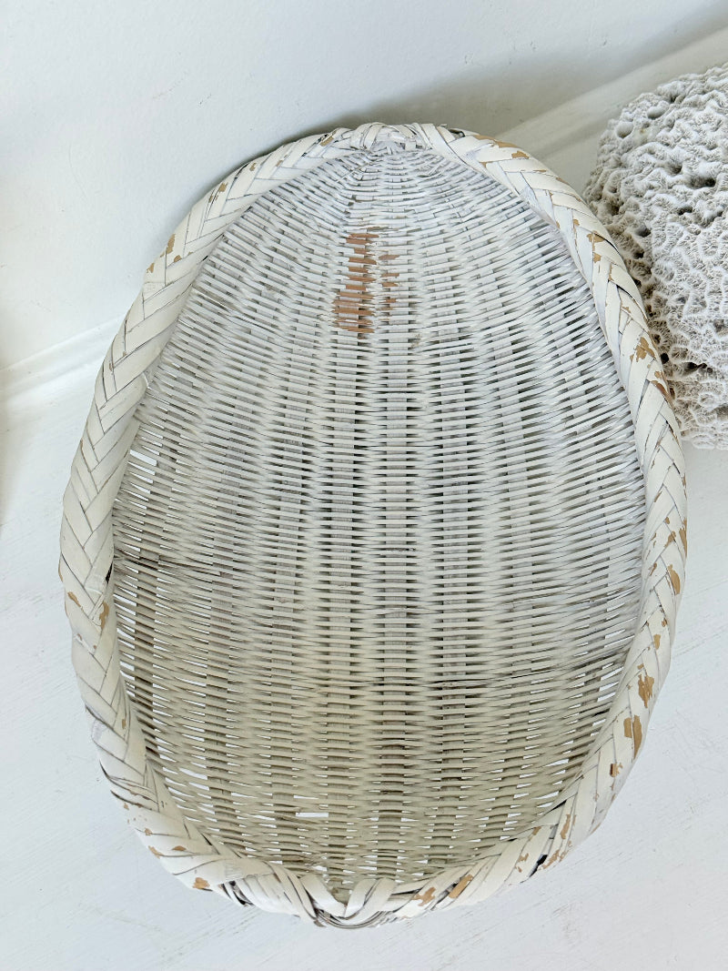 Vintage white chippy wicker basket with oval shape and worn painted finish, photographed on white surface.