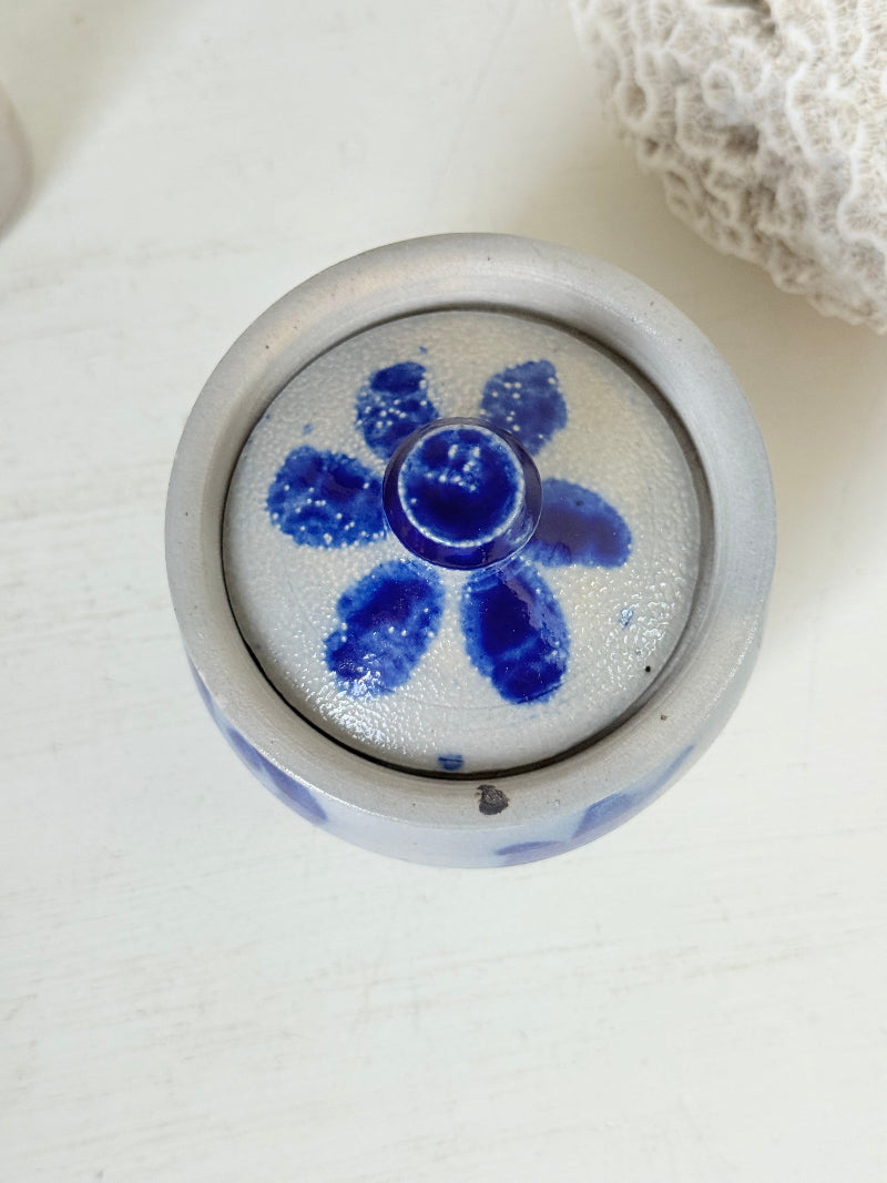 Vintage lidded pottery jar with hand painted blue floral decoration, photographed on a white surface