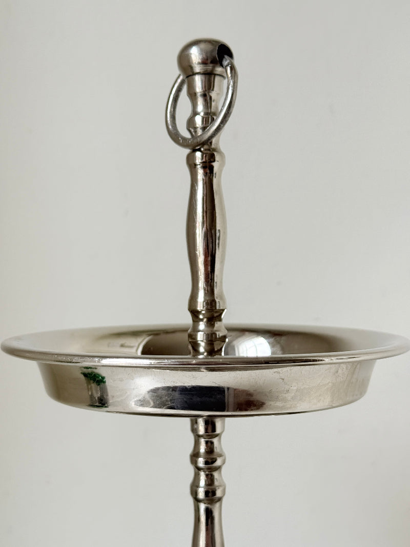 Two tier silver tone cake stand with polished reflective finish styled with green wrapped sweets on a white surface