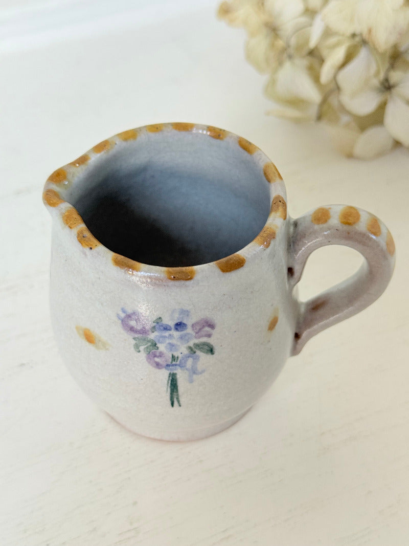 vintage studio pottery milk jug with hand painted lilac flowers and ochre rim photographed on white surface