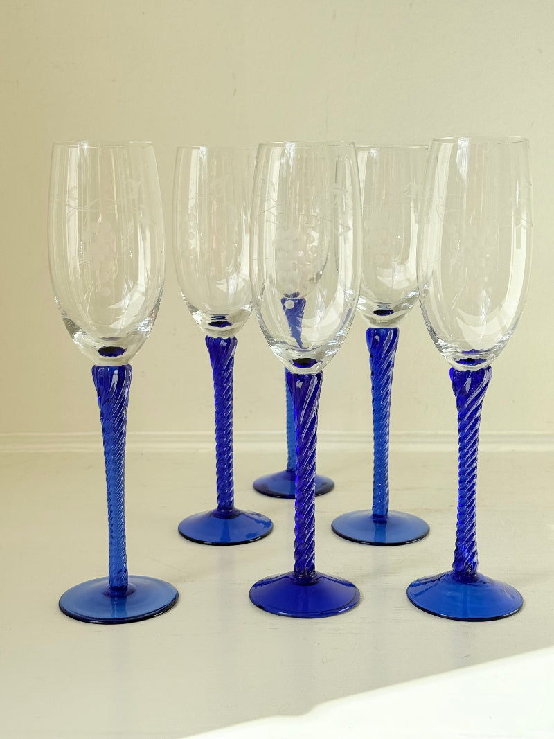 Set of six vintage French champagne flutes with tall clear bowls and cobalt blue twisted stems, photographed on white surface.