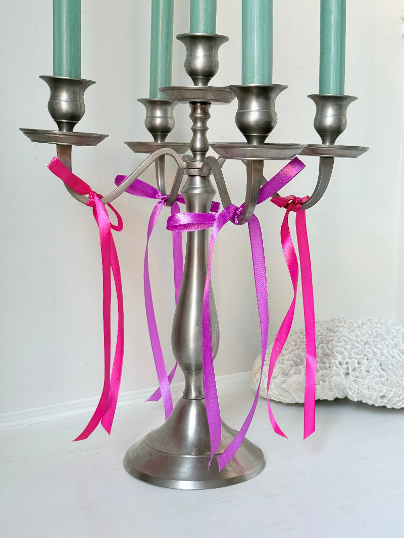 Five arm pewter style metal candelabra with aged silver finish styled with blue green taper candles on white surface